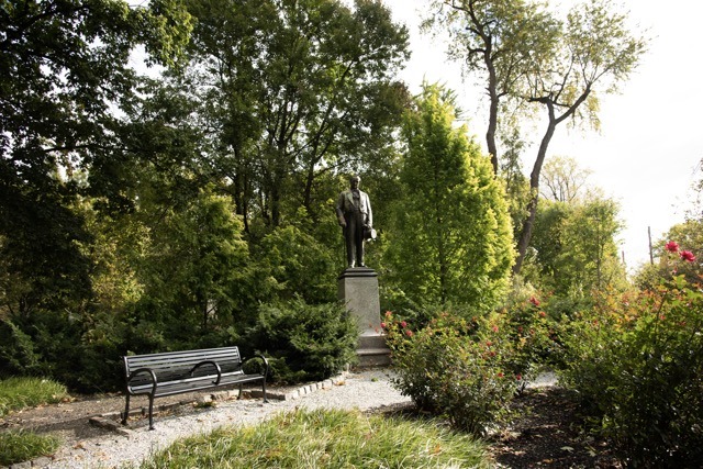 Park with trees, shrubs, park bench, and statue of a man