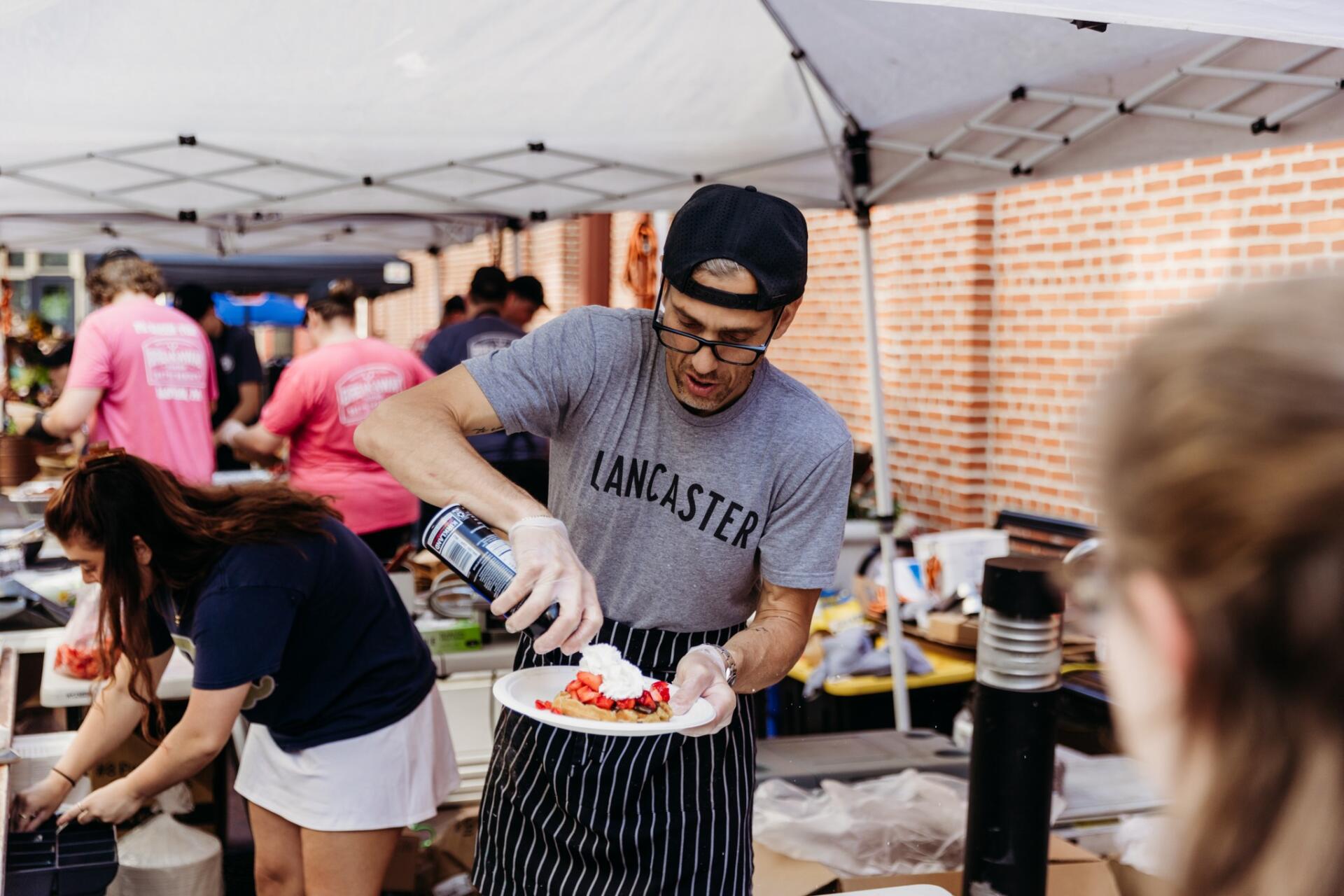 Person putting whipped cream on a strawberry dessert
